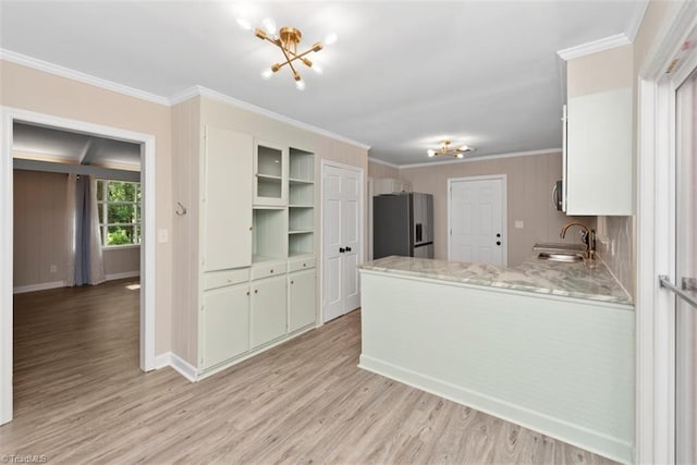 kitchen with stainless steel fridge, a sink, crown molding, light wood-type flooring, and a peninsula