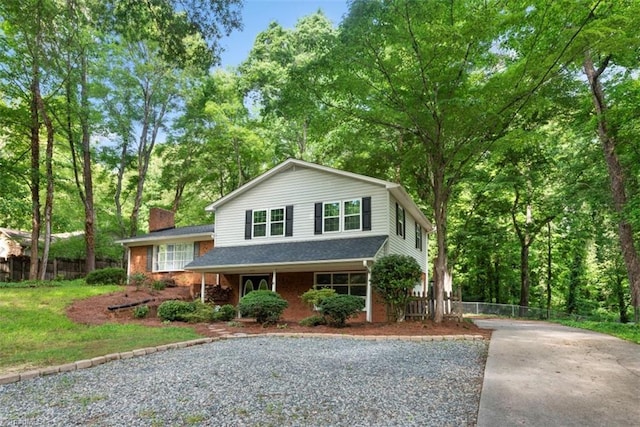 tri-level home with concrete driveway, fence, a chimney, and brick siding
