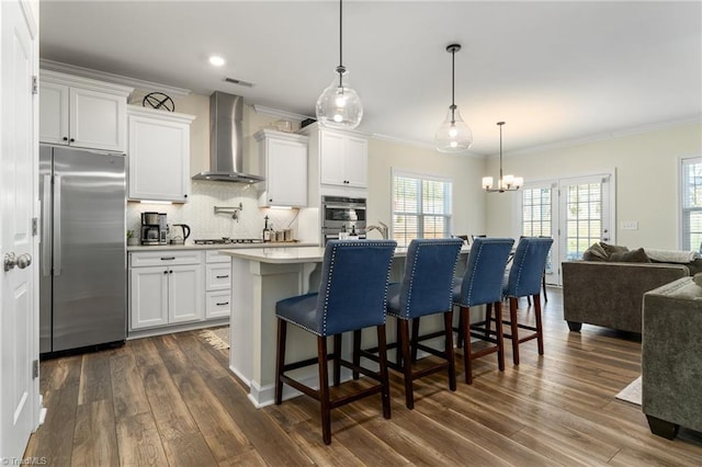 kitchen with white cabinetry, wall chimney range hood, an island with sink, and stainless steel built in refrigerator