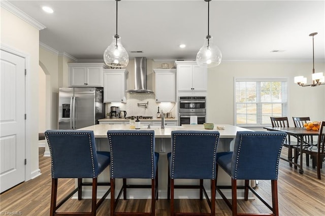 kitchen with white cabinetry, stainless steel appliances, a kitchen bar, and wall chimney range hood