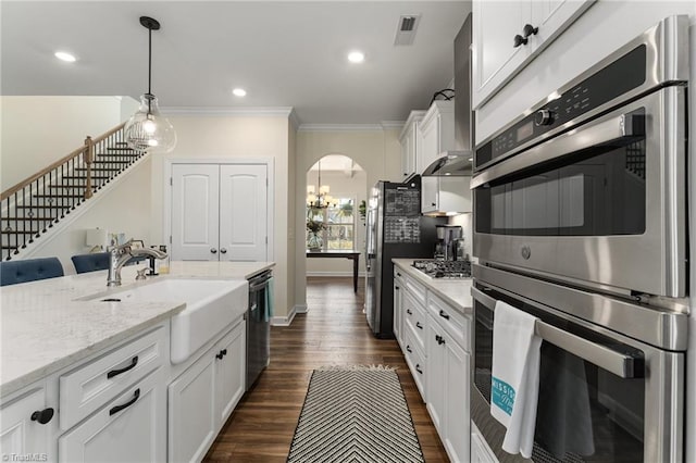 kitchen featuring white cabinetry, decorative light fixtures, ornamental molding, appliances with stainless steel finishes, and light stone countertops