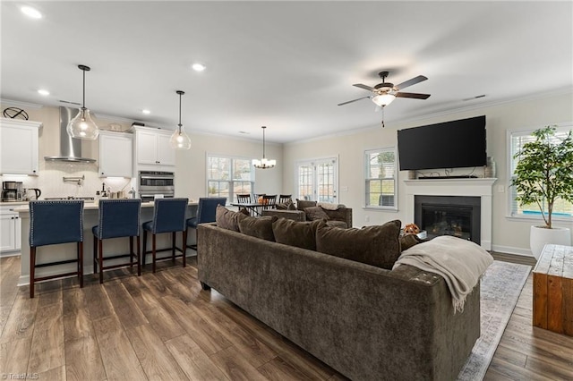 living room featuring dark hardwood / wood-style flooring, ceiling fan with notable chandelier, and ornamental molding