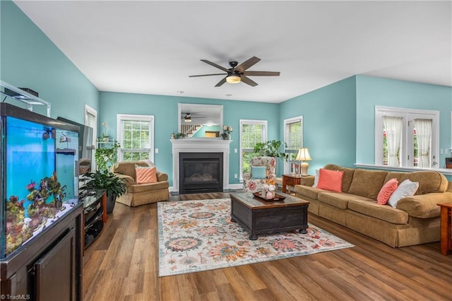 living room with light wood-type flooring, a glass covered fireplace, a ceiling fan, and a healthy amount of sunlight