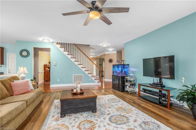 living area featuring baseboards, visible vents, ceiling fan, stairway, and wood finished floors