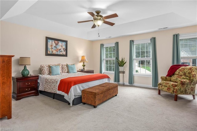 bedroom featuring baseboards, visible vents, a ceiling fan, light colored carpet, and a tray ceiling