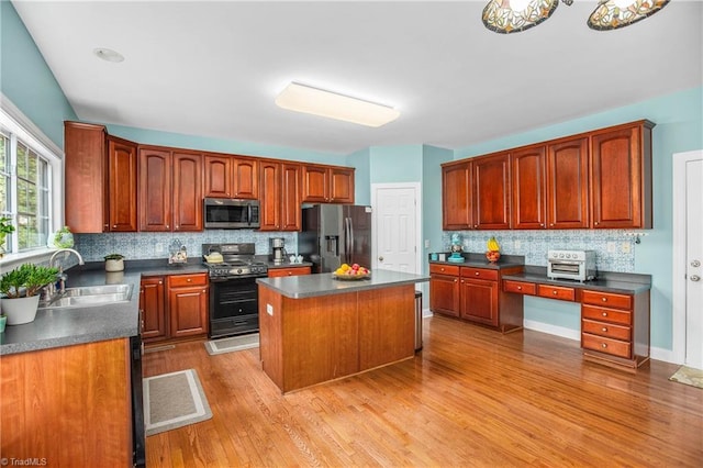 kitchen with dark countertops, a kitchen island, appliances with stainless steel finishes, a sink, and backsplash