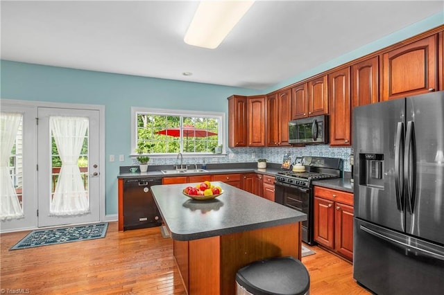 kitchen featuring tasteful backsplash, dark countertops, a sink, a kitchen island, and black appliances