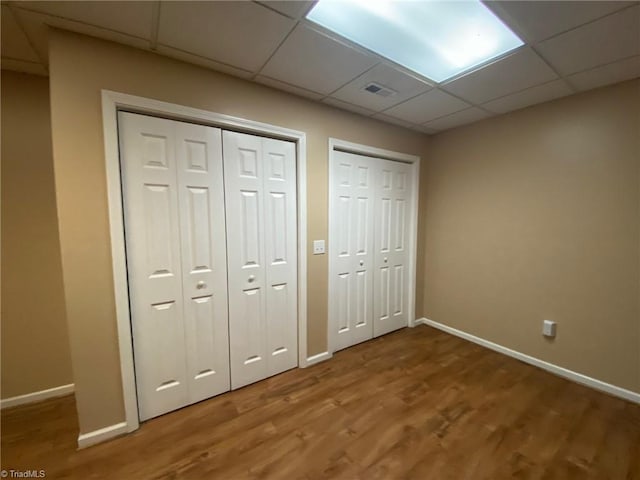 unfurnished bedroom with hardwood / wood-style flooring, a drop ceiling, and two closets