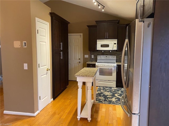 kitchen with vaulted ceiling, decorative backsplash, dark brown cabinetry, white appliances, and light hardwood / wood-style flooring