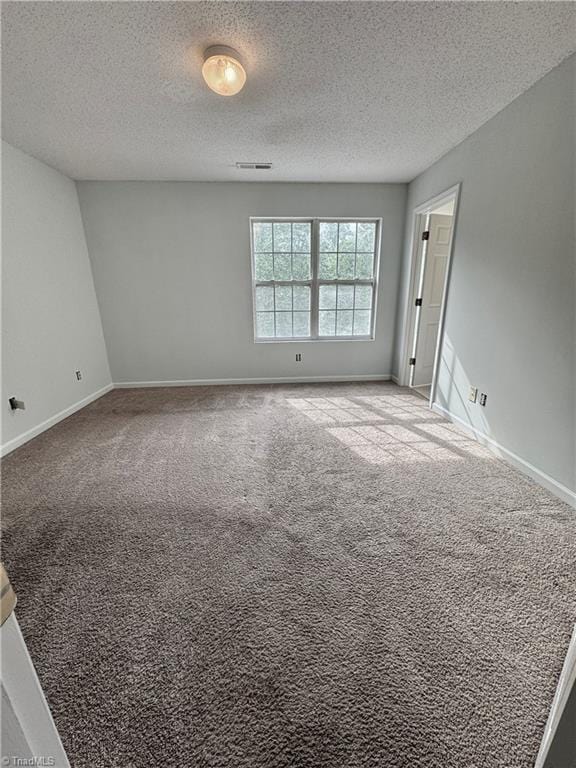 carpeted spare room featuring a textured ceiling and baseboards