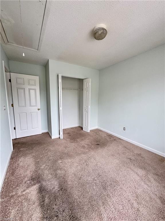 unfurnished bedroom with attic access, carpet floors, a closet, baseboards, and a textured ceiling