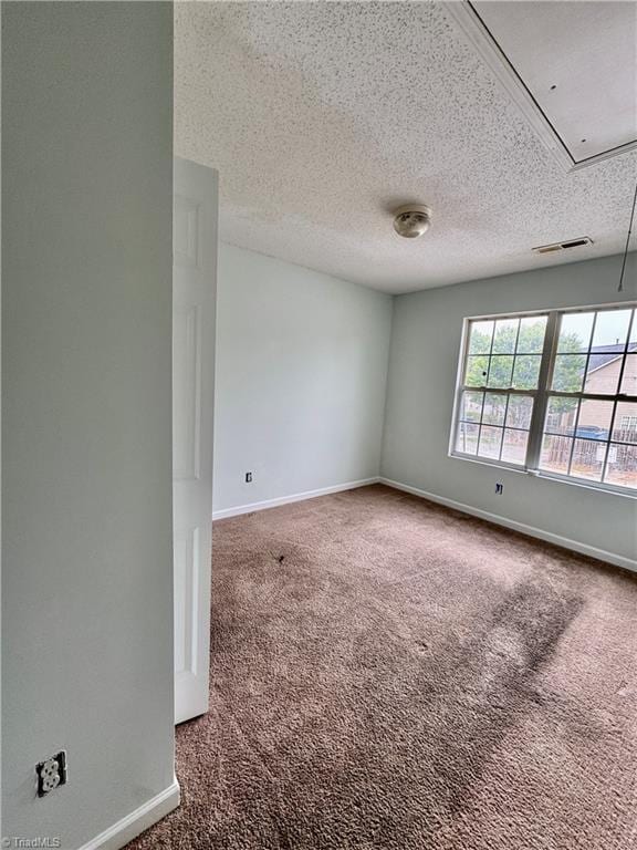 empty room with attic access, carpet, a textured ceiling, and baseboards