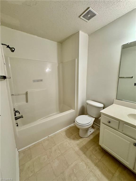 full bathroom featuring toilet, a textured ceiling, vanity, and tub / shower combination