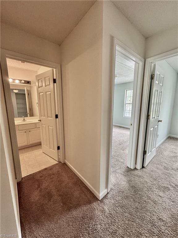 corridor featuring light carpet, baseboards, and a sink