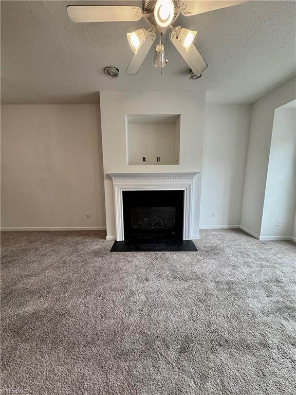unfurnished living room featuring a ceiling fan, a textured ceiling, a fireplace with flush hearth, baseboards, and carpet floors