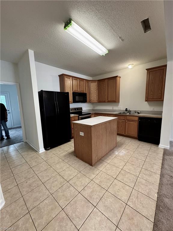 kitchen with black appliances, a sink, a center island, a textured ceiling, and light tile patterned floors