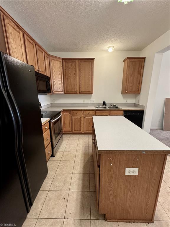 kitchen with black appliances, a textured ceiling, a sink, light countertops, and light tile patterned floors