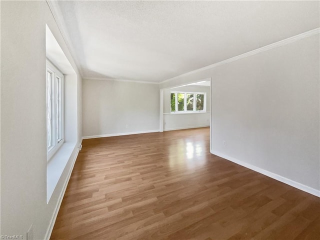 spare room featuring crown molding, baseboards, and wood finished floors