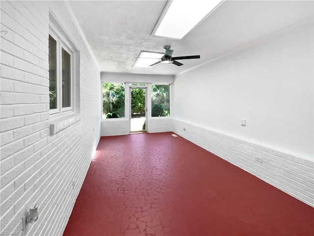 unfurnished room with a ceiling fan, brick wall, and a skylight