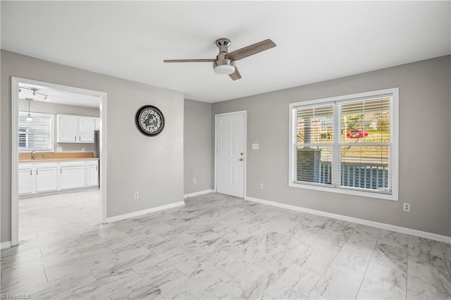 unfurnished room with ceiling fan, marble finish floor, a sink, and baseboards