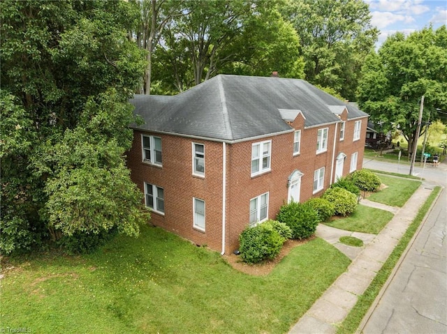 view of side of home with a garage, brick siding, a yard, and driveway