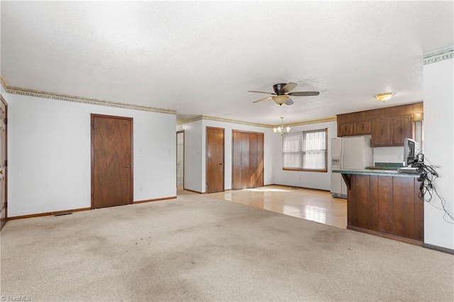 unfurnished living room with ceiling fan with notable chandelier, a textured ceiling, crown molding, baseboards, and light colored carpet