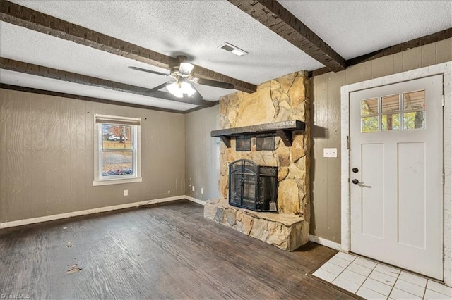 unfurnished living room featuring hardwood / wood-style floors, a wealth of natural light, beamed ceiling, and a stone fireplace