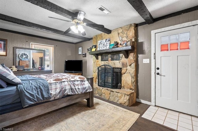 tiled bedroom with a textured ceiling, ceiling fan, beam ceiling, and a stone fireplace