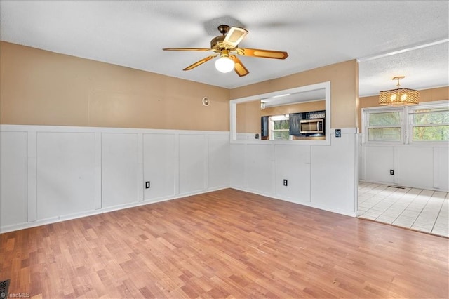 empty room with ceiling fan, a textured ceiling, and light hardwood / wood-style floors