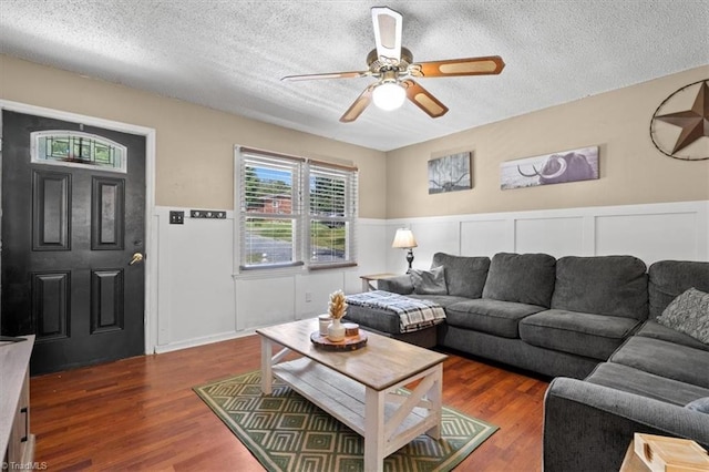 living room featuring dark wood-type flooring, ceiling fan, and a textured ceiling