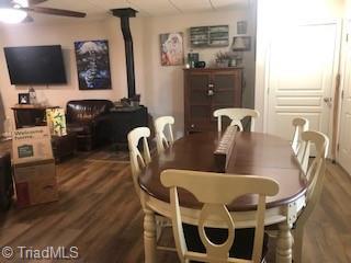 dining space with wood finished floors, a wood stove, and a ceiling fan