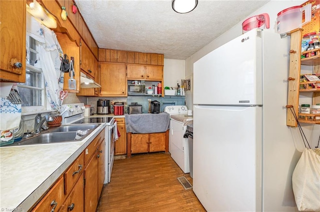 kitchen with under cabinet range hood, white appliances, a sink, light countertops, and brown cabinets