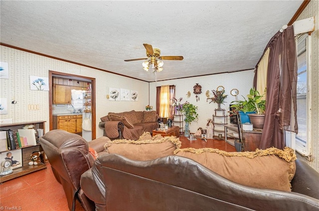 living area with ornamental molding, ceiling fan, a textured ceiling, and wallpapered walls