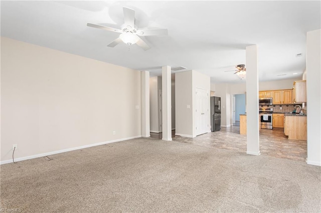 unfurnished living room featuring a ceiling fan, visible vents, baseboards, a sink, and light colored carpet