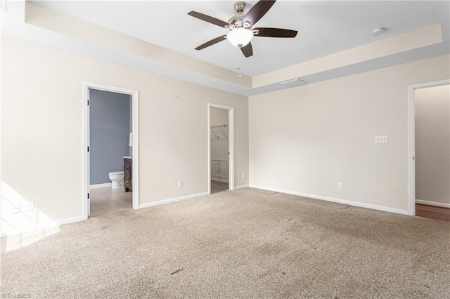 unfurnished bedroom with visible vents, baseboards, carpet floors, ensuite bath, and a tray ceiling