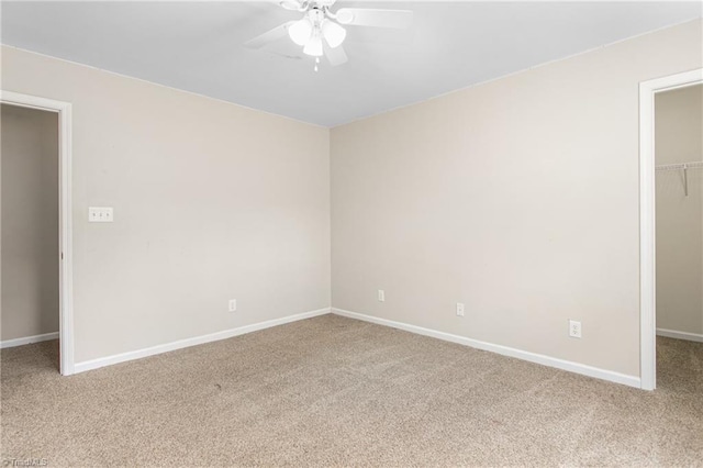 unfurnished bedroom with a walk in closet, a ceiling fan, a closet, carpet flooring, and baseboards