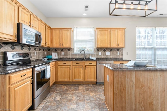 kitchen with visible vents, a sink, appliances with stainless steel finishes, stone finish flooring, and tasteful backsplash