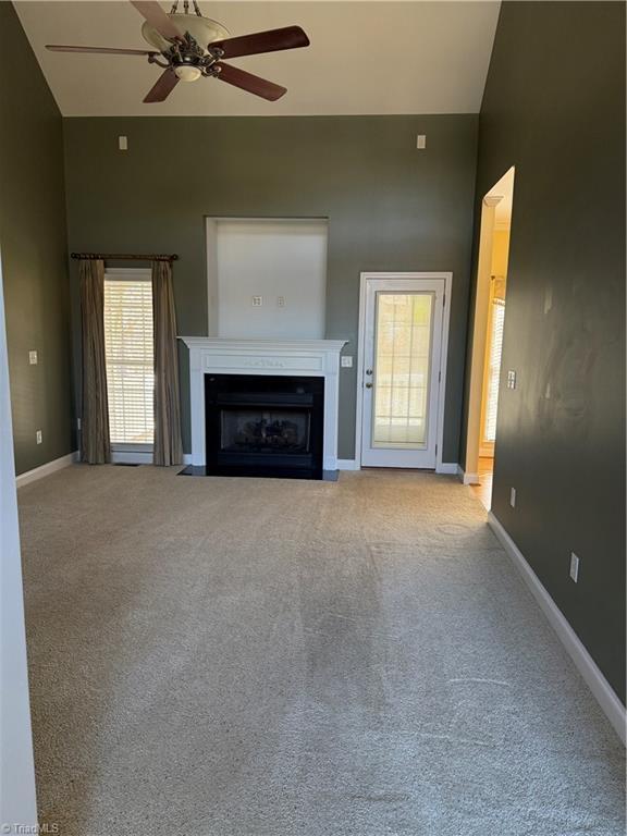 unfurnished living room featuring a fireplace with flush hearth, carpet, ceiling fan, and baseboards