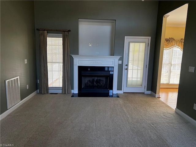 unfurnished living room with carpet floors, baseboards, visible vents, and a fireplace with flush hearth