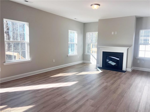 unfurnished living room with visible vents, baseboards, wood finished floors, and a fireplace with flush hearth