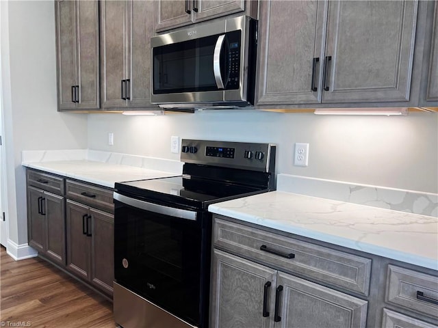 kitchen with dark hardwood / wood-style floors, appliances with stainless steel finishes, dark brown cabinets, and light stone counters