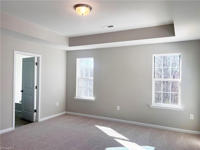 carpeted empty room featuring visible vents, a tray ceiling, and baseboards