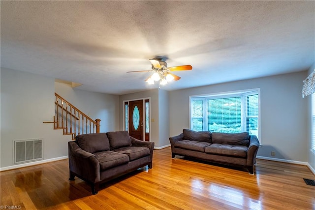 living room with ceiling fan, light wood-type flooring, and a textured ceiling