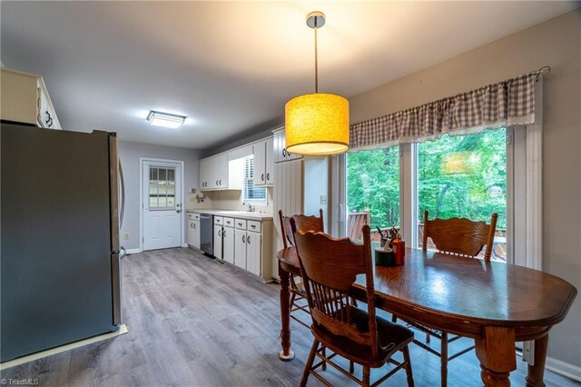 kitchen featuring white cabinets, light wood-type flooring, decorative light fixtures, and stainless steel dishwasher