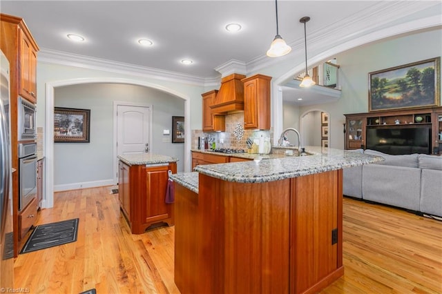 kitchen featuring kitchen peninsula, light wood-type flooring, light stone counters, sink, and pendant lighting