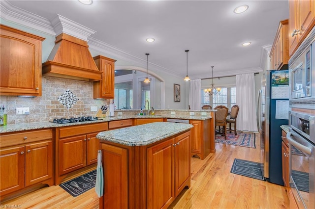 kitchen featuring appliances with stainless steel finishes, decorative light fixtures, a kitchen island, and light hardwood / wood-style floors