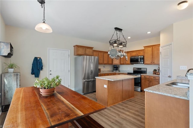 kitchen featuring pendant lighting, sink, appliances with stainless steel finishes, light stone counters, and wood-type flooring