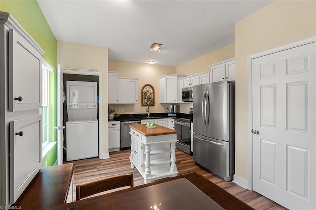 kitchen with dark wood-type flooring, white cabinetry, stainless steel appliances, stacked washer / dryer, and wood counters