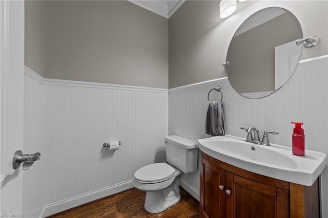 half bath with wainscoting, vanity, toilet, wood finished floors, and ornamental molding