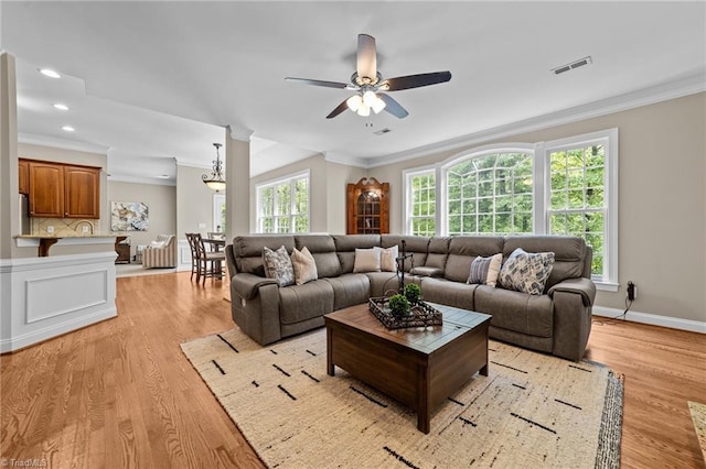 living area featuring visible vents, light wood-style floors, crown molding, and ceiling fan